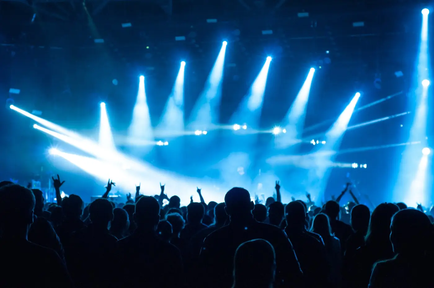 Crowd with hands raised under blue stage beams